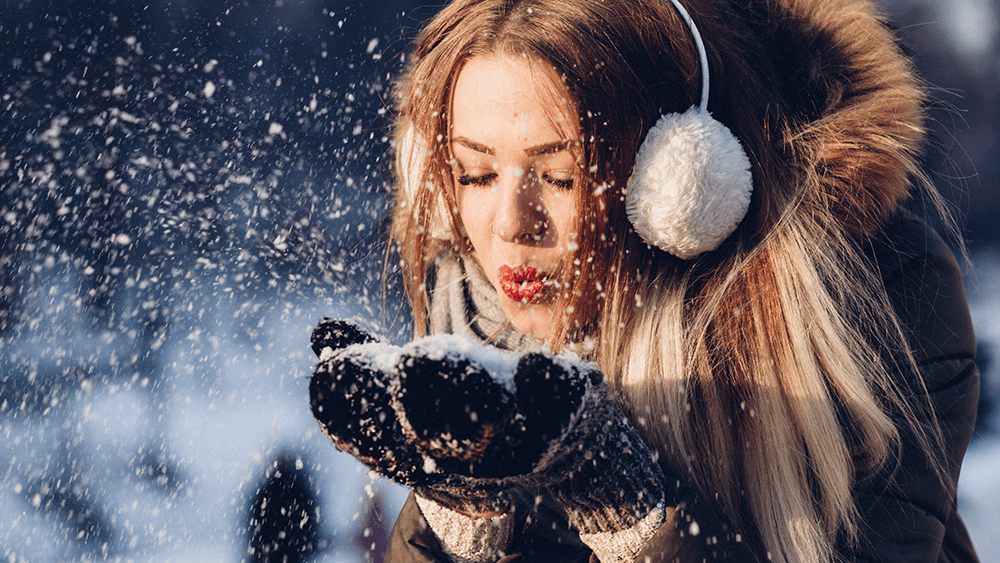 Woman blowing snow with earmuffs